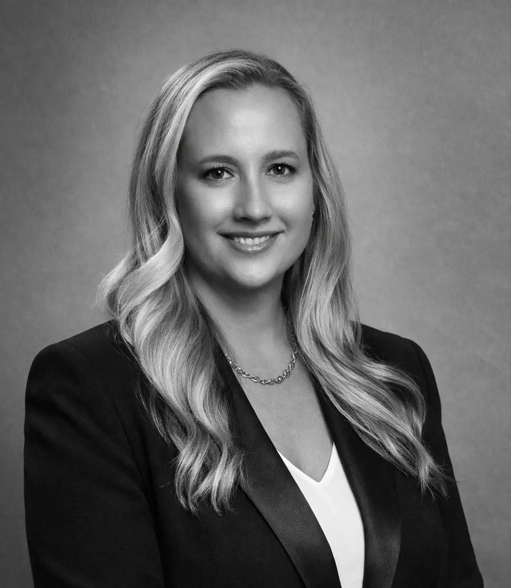 Black and white portrait of a woman with long, wavy hair, wearing a blazer over a white top and a chain necklace, facing the camera and smiling slightly—embodying the elegance of luxury surface specification.