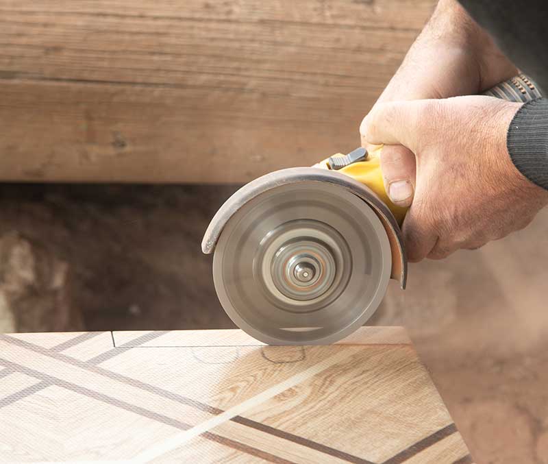 A person uses a circular saw to cut a piece of patterned wood, with the blade in motion and sawdust visible—demonstrating precision craftsmanship suitable for luxury surface specification projects.
