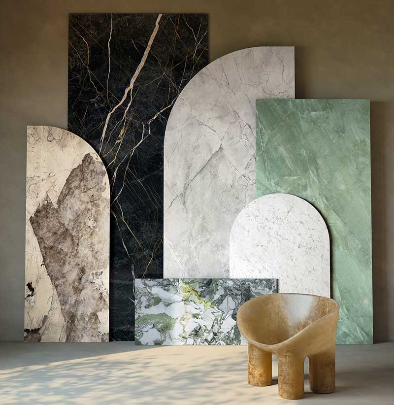 Six large marble slabs from a high-end stone supplier in various colors and shapes are arranged vertically against a wall; a sculptural tan chair sits in the foreground.