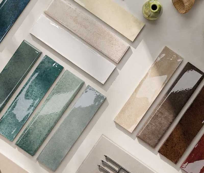 Rectangular ceramic tiles in various colors and finishes are arranged on a flat surface alongside small decorative items, showcasing the refined selection of a premium tile Florida distributor.